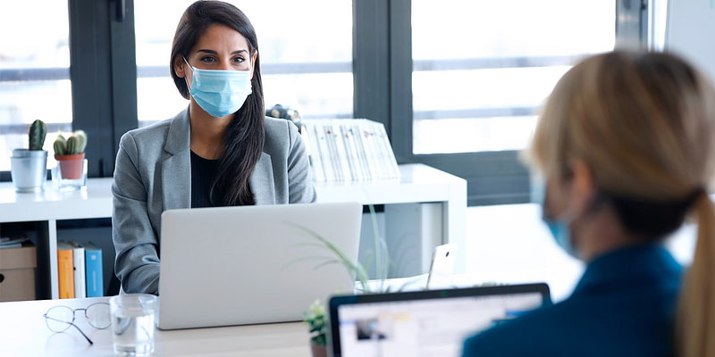 Two businesswomen wearing masks as the share a co-working station