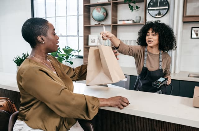 Customer receiving a paper bag while making a card payment at a modern store counter