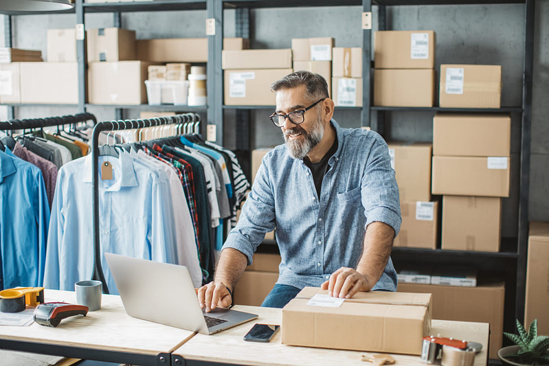 Mature, small business owner, preparing packages to be sent out using a laptop.