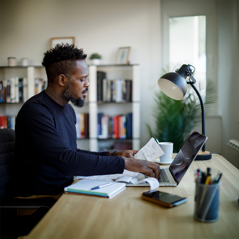 a man looking at some papers and working on a laptop
