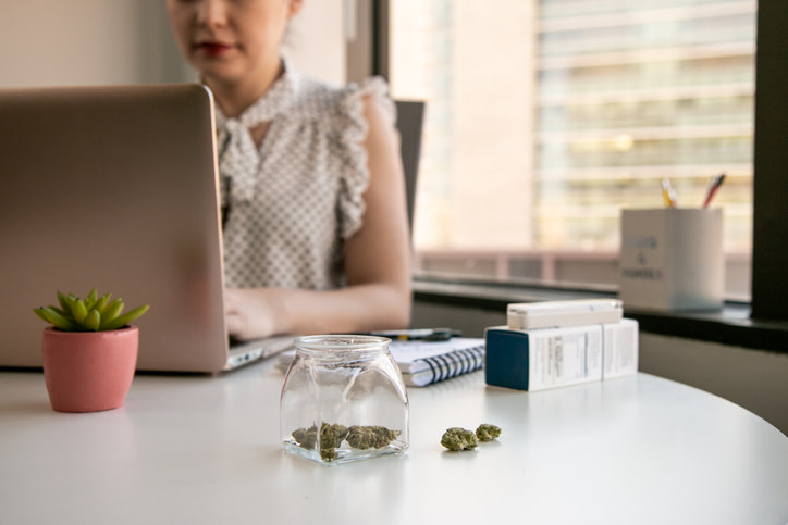 a woman sits in her workplace with a jar of cannabis on her desk