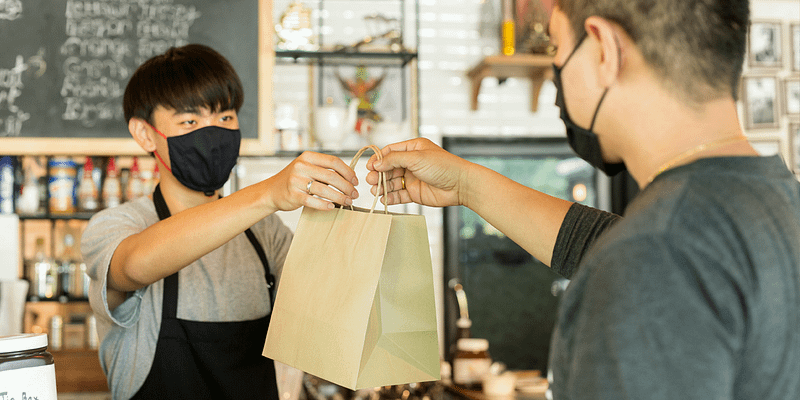 small business owner with face mask is handing a customer their purchase