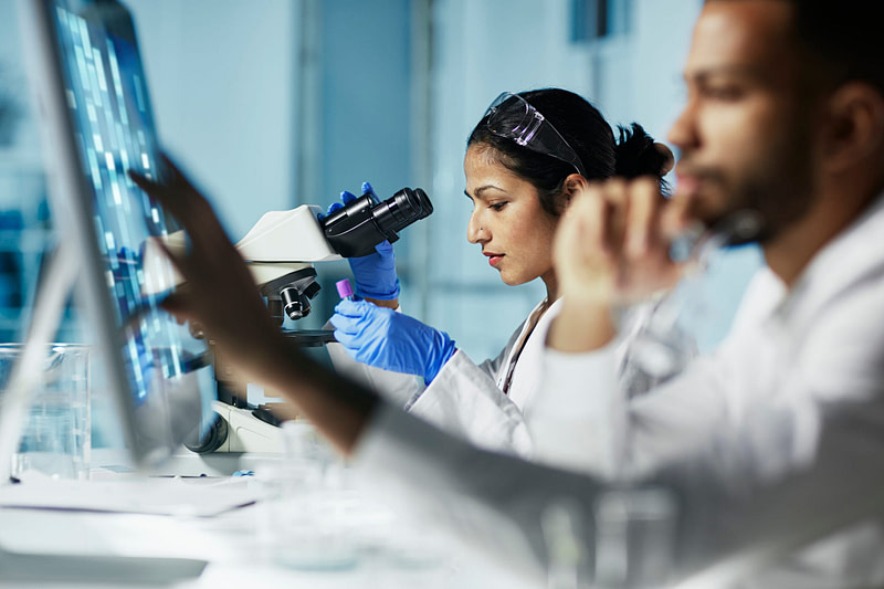 Woman working in a modern lab facility with a microscope and specimen.